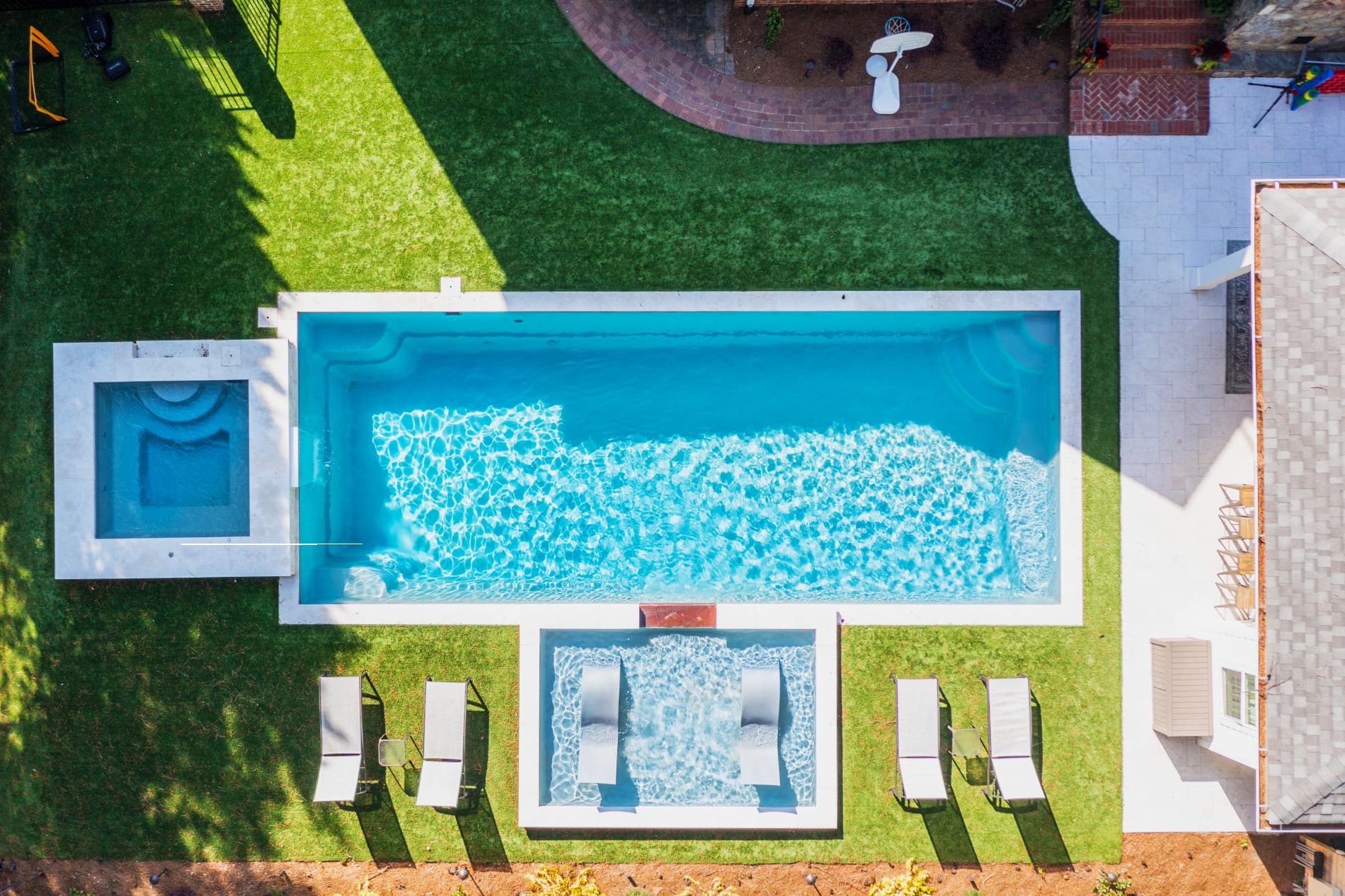 Swimming pool with spillway and TL15 with spillway in Granite Gray with bubblers, turf patio and natural stone coping